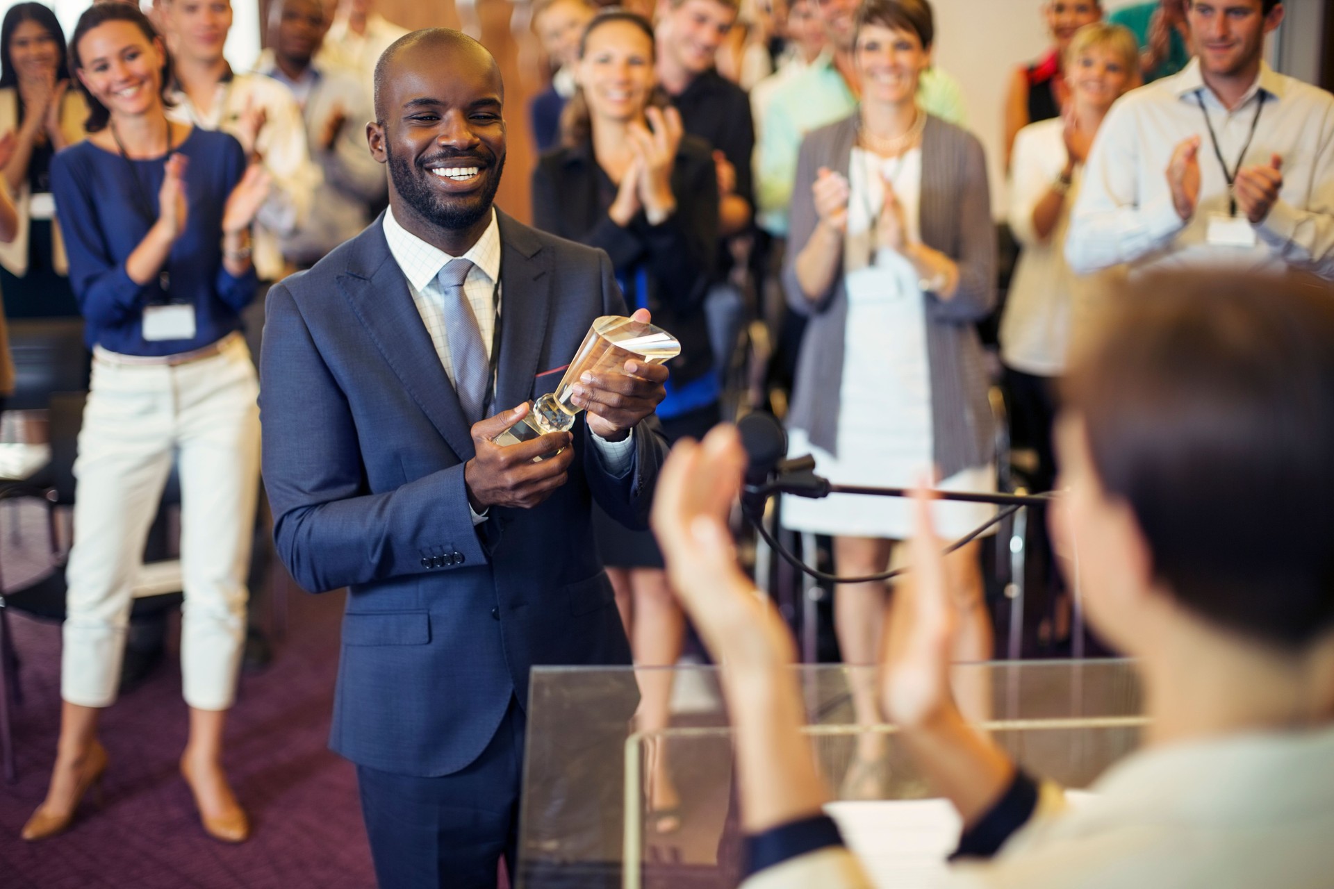 Portrait of young man holding trophy, standing in conference room, smiling to applauding audience